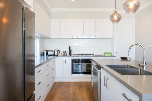 a kitchen with white cabinets and a stainless steel refrigerator at La Vista - Water Views & Mountain Vistas in Culburra Beach