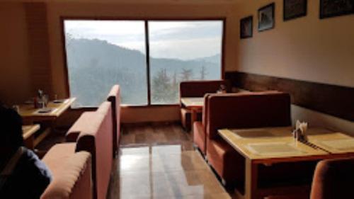 un restaurant avec des tables et des chaises et une grande fenêtre dans l'établissement Shimla Greens Shimla, à Shimla