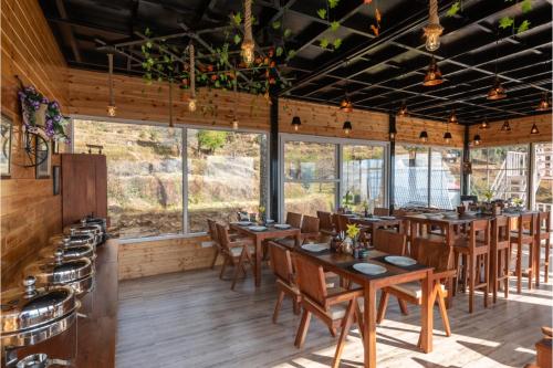 un restaurante con mesas y sillas de madera y ventanas en Vinyasa Resort , Kanatal, en Kanatal