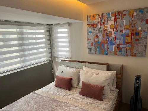 a bedroom with a bed with two pillows and a painting at Fort Victoria Loft in BGC Wifi Netflix in Manila