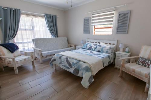 a bedroom with a bed and a chair and windows at Surf n Sea Beachfront Holiday Home in Jeffreys Bay