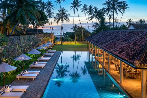 a hotel pool with lounge chairs and umbrellas at Taru Villas The Long House - Bentota in Bentota