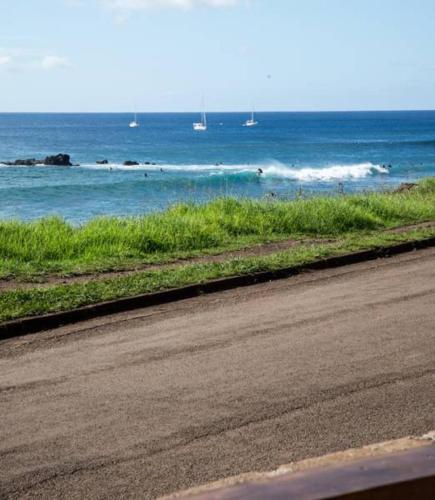 a road next to the ocean with boats in the water at PARAÍSO Sunset Bungalows in Hanga Roa