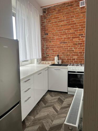 uma cozinha com armários brancos e uma parede de tijolos em apartament em Skarżysko-Kamienna