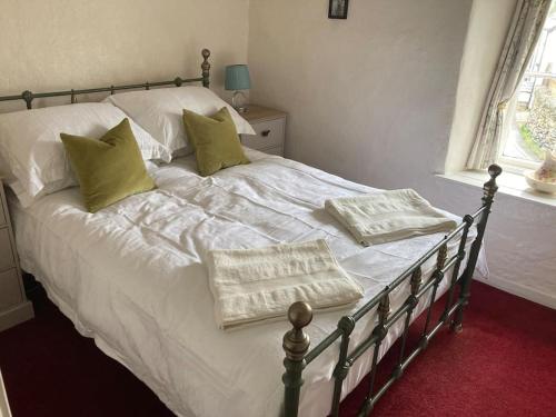 a bed with white sheets and green pillows on it at Lovely peaceful 2 bed cottage in Llandderfel