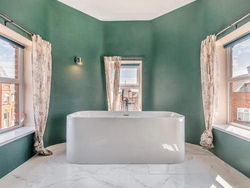 a white tub in a green bathroom with two windows at 7 Bed in Bridlington 90787 in Bridlington