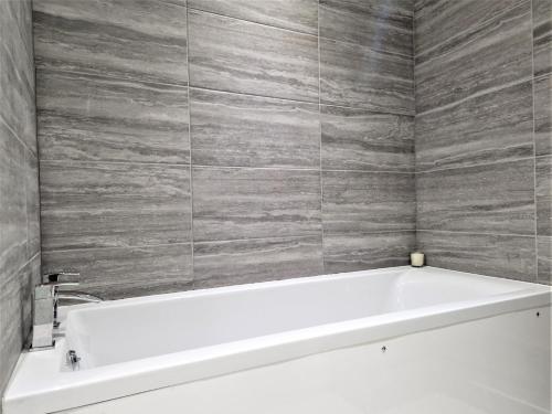 a white bath tub in a bathroom with gray tiles at 2 bed property in Gunnislake Cornwall 90781 in Gunnislake