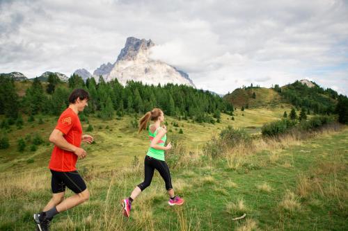 two people running in a field with a mountain in the background at Naturae Lodge Wellness & Spa in Alleghe