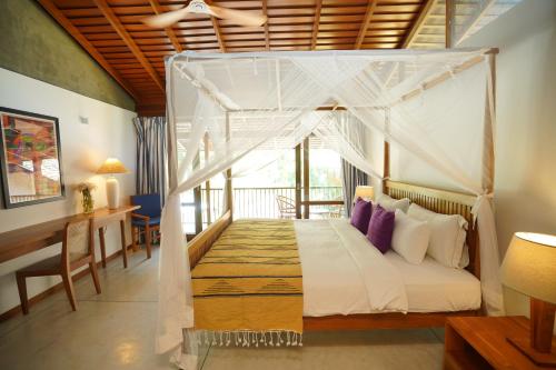 a bedroom with a canopy bed and a desk at Maison Samara in Hikkaduwa