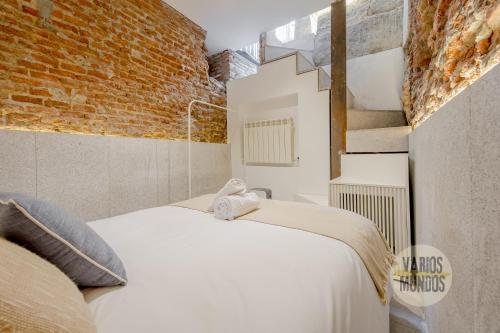 a bedroom with a white bed and a brick wall at Cool Duplex Bajo Apt 7pax cerca de Tirso de Molina in Madrid