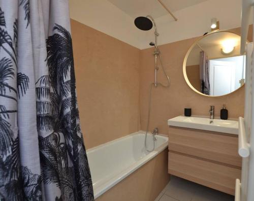 une salle de bain avec une baignoire, un lavabo et un miroir dans l'établissement Le Mayflower sous les palmiers, au Grau-du-Roi