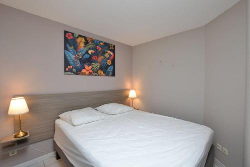 une chambre avec un lit blanc et un tableau au mur dans l'établissement Le Mayflower sous les palmiers, au Grau-du-Roi