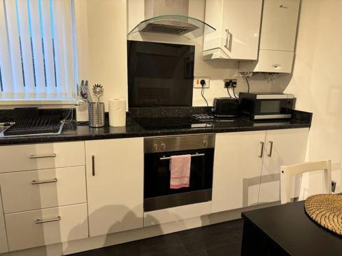 een keuken met witte kasten en een zwarte oven bij Summer House Sleeps 6 , 2 Large Parking Spaces, walking distance to Cardiff Bay and City Centre in Cardiff