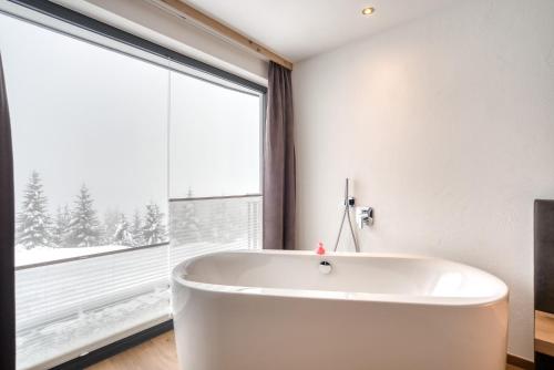a white bath tub in a bathroom with a large window at Ursprung Panorama Hotel Königsleiten in Königsleiten