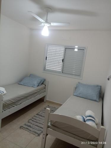 two beds in a room with a fan and a window at AP da Karine a 700 metros da praia da Guilhermina in Praia Grande