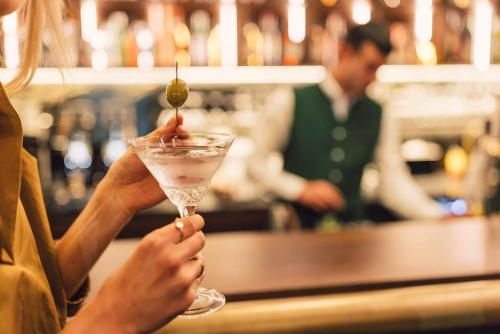 a woman holding a drink with a olive on it at Posthotel Taube in Schruns-Tschagguns