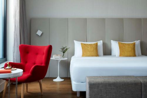 フランクフルト・アム・マインにあるAvani Frankfurt City Hotel - previously NH Collection Frankfurt Cityのベッドと赤い椅子が備わるホテルルームです。