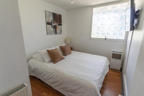 Cama blanca en habitación pequeña con ventana en Kennedy Apartments Los Militares, en Santiago