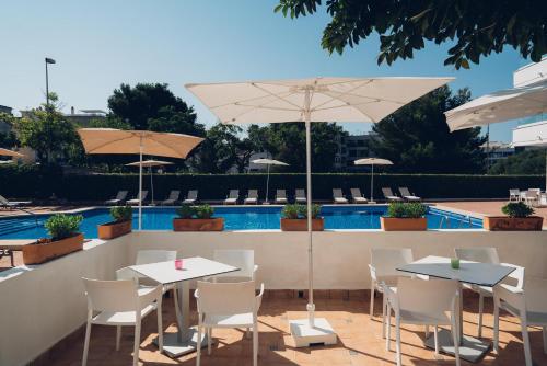 two tables and chairs with umbrellas next to a pool at THB Dos Playas - Adults Only in Cala Ratjada