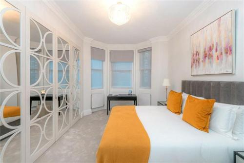 ein weißes Schlafzimmer mit einem großen Bett mit orangefarbenen Kissen in der Unterkunft Belgravia/Victoria Border Luxury House Sleeps 8 comfortably in London