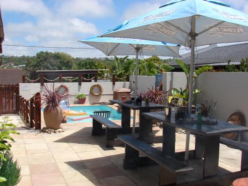 two picnic tables with an umbrella next to a pool at A Time And A Place in Plettenberg Bay