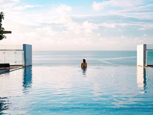 un hombre sentado en una piscina con vistas al océano en ibis Styles Vung Tau en Vung Tau