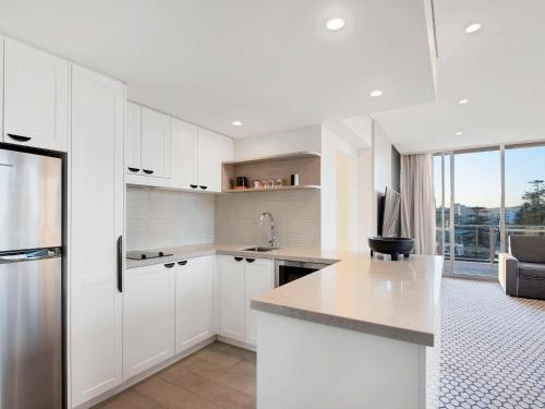 a kitchen with white cabinets and a large window at Peppers Manly Beach in Sydney