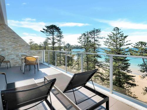 a balcony with chairs and a table and a view of the beach at Peppers Manly Beach in Sydney