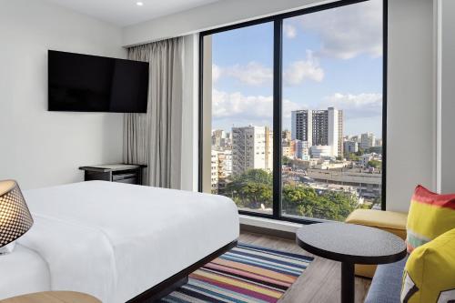 Habitación de hotel con cama blanca y ventana grande. en Aloft Santo Domingo Piantini, en Santo Domingo