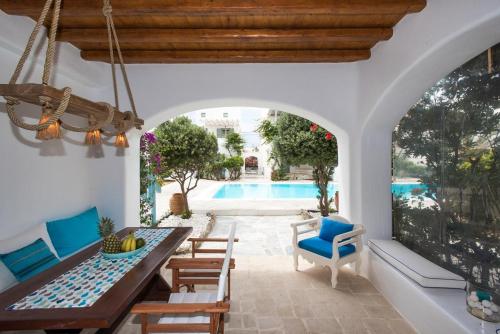 Un patio con mesa y sillas y una piscina. en Mykonian Style w Shared Pool Houses & Nighttime Security Guard, en Ornos