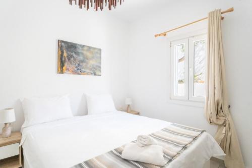 a white bedroom with a white bed and a window at BLUE WATERS MYKONOS in Ornos