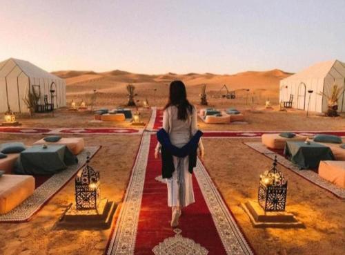 Una mujer caminando sobre una alfombra roja en el desierto en Merzouga Luxury Camp, en Merzouga