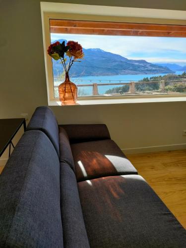 a couch in front of a window with a vase with flowers at Le Panoramique du Plongeoir - T4 spacieux de 90m2 avec grande terrasse vue sur le lac de Serre Ponçon in Savines