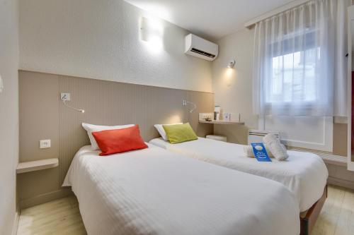 two beds in a room with white sheets and colorful pillows at Brit Hotel Lille Centre in Lille