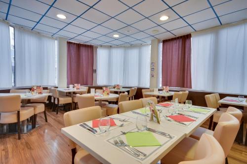 a restaurant with white tables and chairs and windows at Brit Hotel Lille Centre in Lille