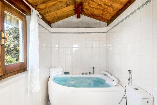 eine Badewanne in einem weiß gefliesten Bad mit einem Fenster in der Unterkunft Vivi Luxury Country House in Comano