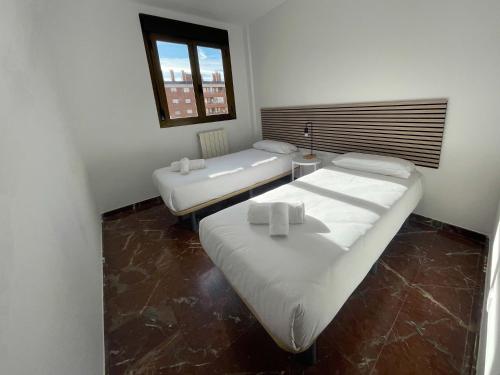 two beds in a small room with a window at Apartamentos El Pilar Suites 3000 in Zaragoza