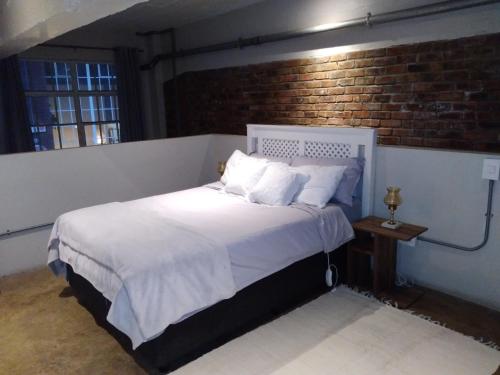 a bedroom with a white bed with a brick wall at House of Cairo - Johannesburg in Johannesburg