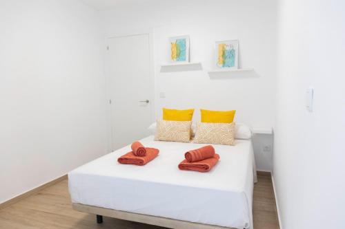 białe łóżko z pomarańczowymi i żółtymi poduszkami w obiekcie Sol y Mar Boutique Apartments w Alicante