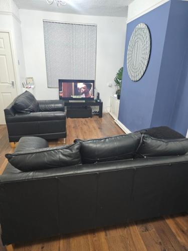 a living room with a black couch and a tv at Your Happy Place-2 Bedroom House in Liverpool