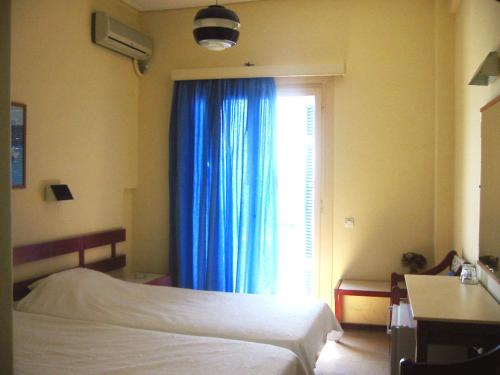 a bedroom with a bed and a window with blue curtains at Hotel Avra in Aegina Town