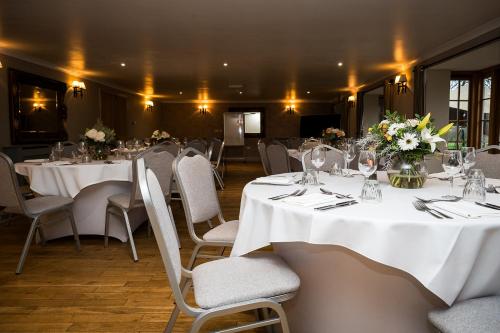 a dining room with white tables and chairs and flowers at Tottington Manor Hotel in Henfield