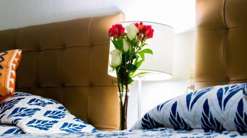 un jarrón con flores rojas y blancas junto a una cama en posada el castellano, en Comitán de Domínguez