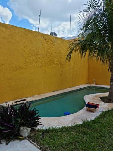 a swimming pool next to a yellow wall with a palm tree at Casa Hacienda Estrada in Campeche