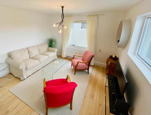 uma sala de estar com um sofá branco e cadeiras vermelhas em Cute Apartment - Detmold city center - large kitchen, bath, south facing balcony - free parking and wifi em Detmold