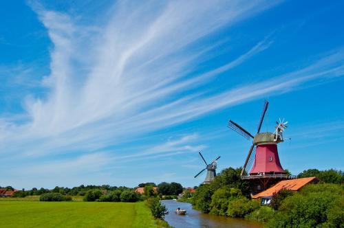 a windmill on the river with a boat in front at Hotel Grachtenhuus Greetsiel in Greetsiel