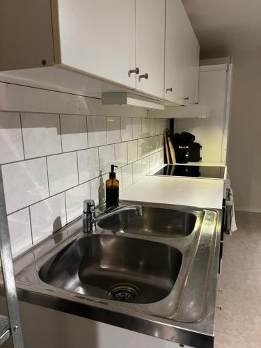 La cuisine est équipée d'un évier en acier inoxydable et de placards blancs. dans l'établissement Mysig lägenhet!, à Göteborg