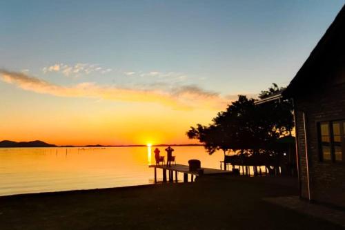 a sunset over the water with two people standing on a dock at Chalé Sol Nascente in Imaruí