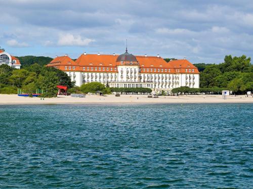 a large white building with red roofs next to the water at Sofitel Grand Sopot in Sopot