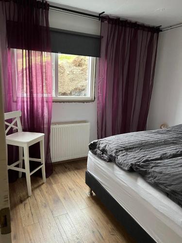 a bedroom with purple curtains and a bed and a chair at Lakeside Apartments in Egilsstadir